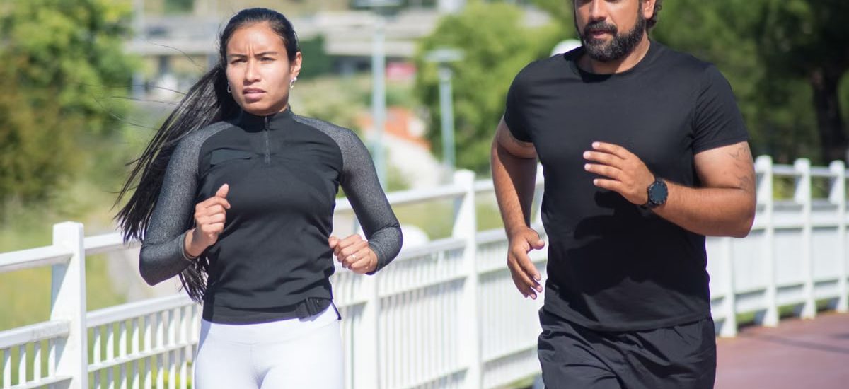 Active couple jogging outdoors on a sunny day, promoting fitness and healthy lifestyle.