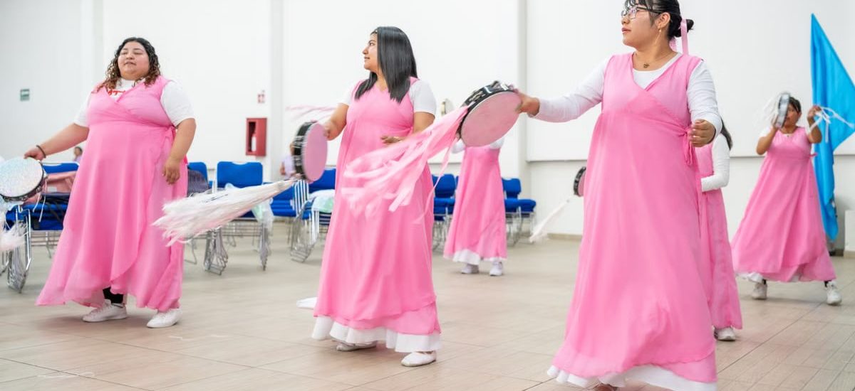 A group of women in pink dresses performing a dance indoors in Mexico City, vibrant and lively.
